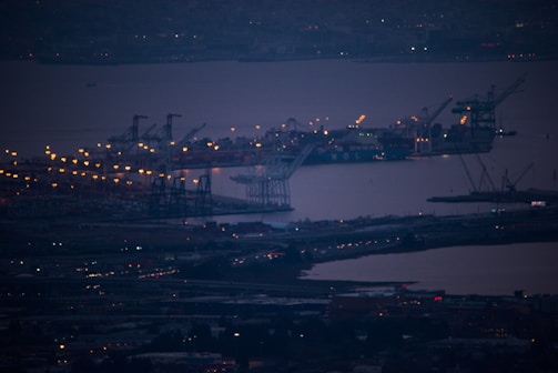 A sprawling port at dusk with cargo ships being loaded under navy and brass lighting.