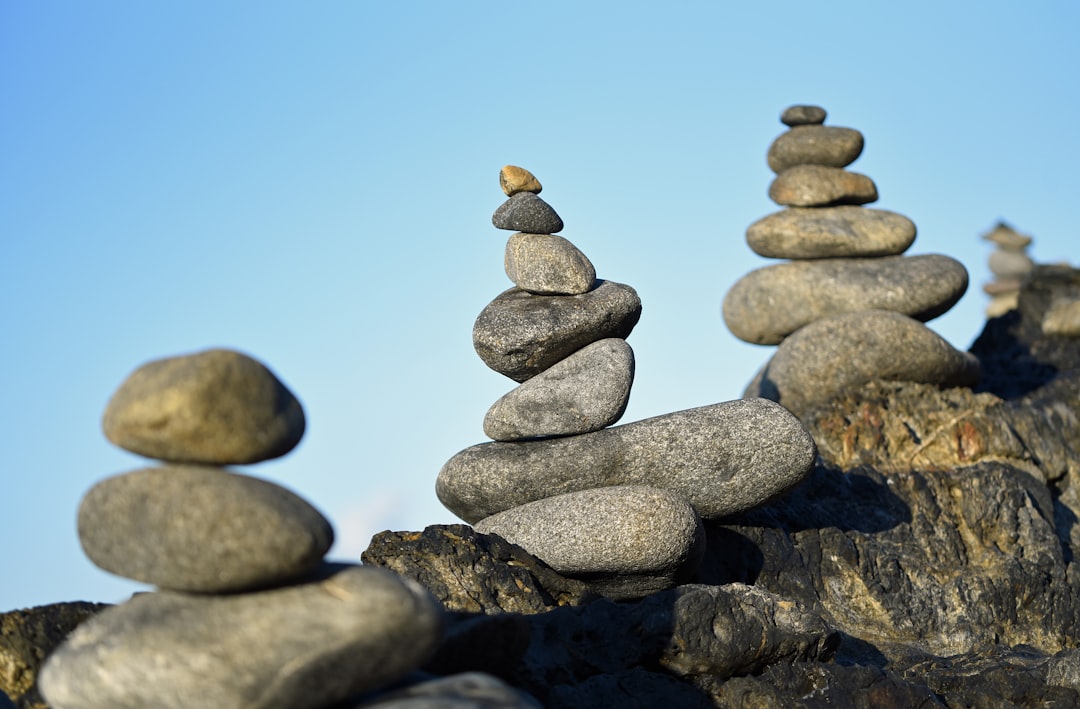 Photo by David Clode of rock cairn rock piles against a pale blue sky