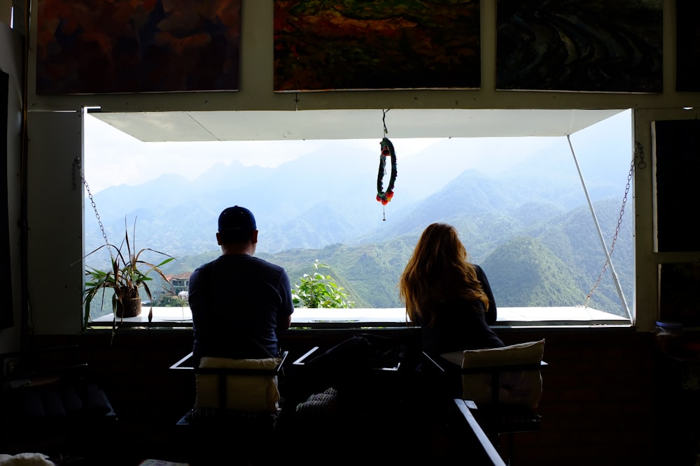 hombre y mujer dentro de la habitación frente a la ventana viendo montañas