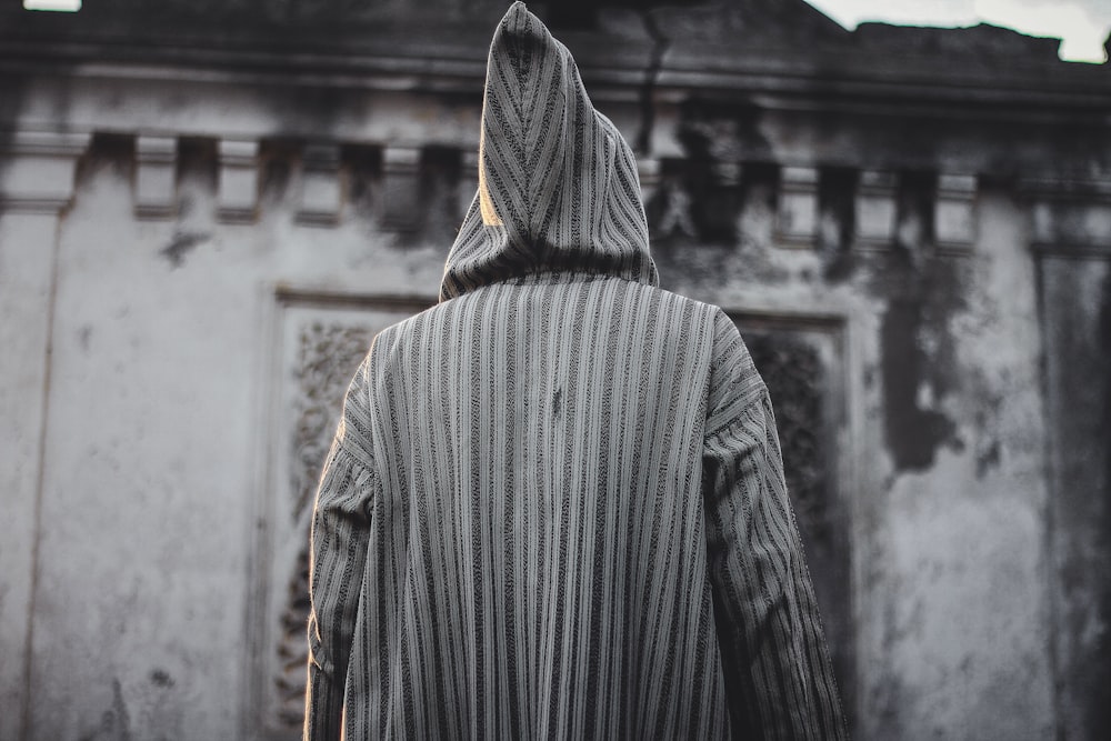 person wearing hoodie standing in front of building grayscale photo