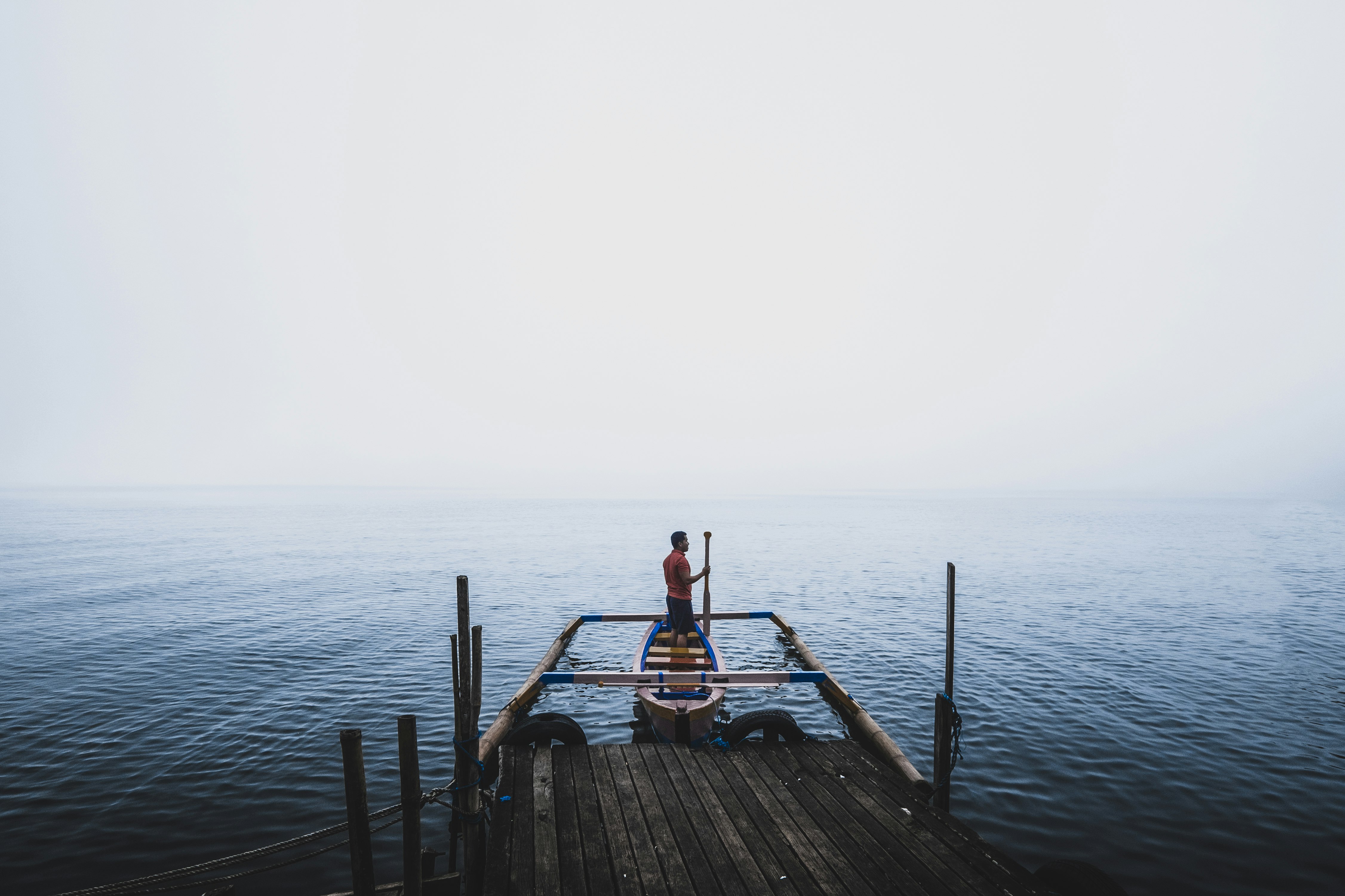 man standing on canoe near dock during daytime