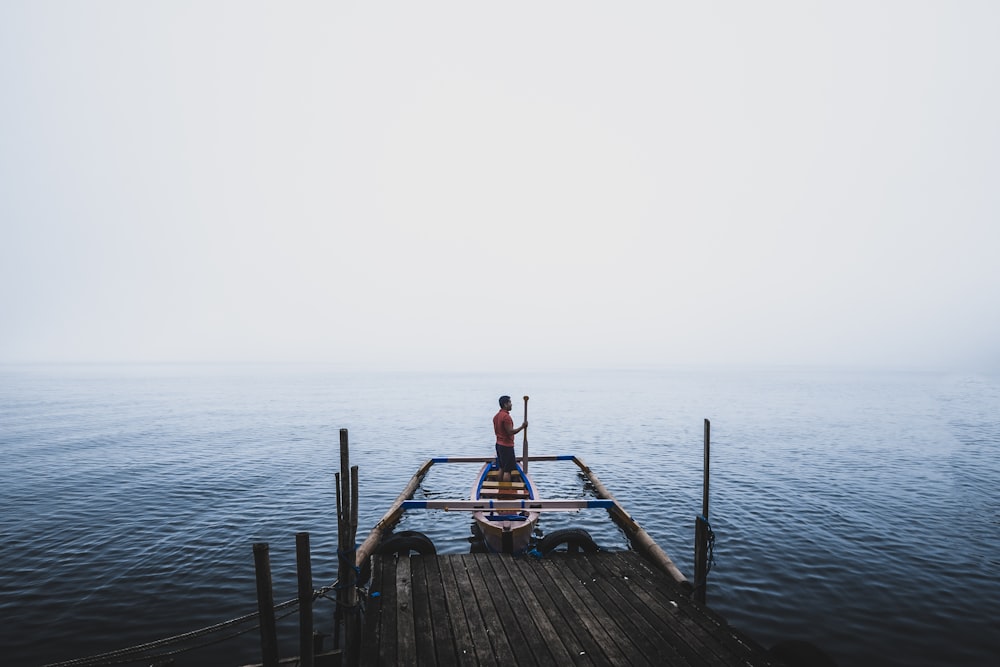 man standing on canoe near dock during daytime