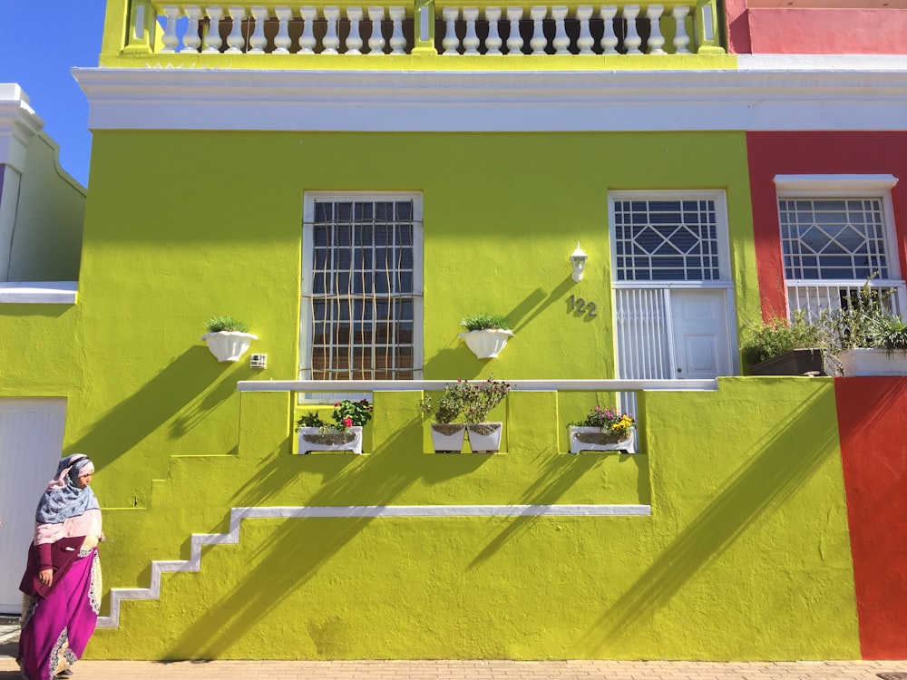 woman walking beside green and red concrete house during daytime