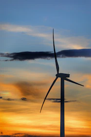A towering wind turbine gracefully turning against a vibrant sunset sky.