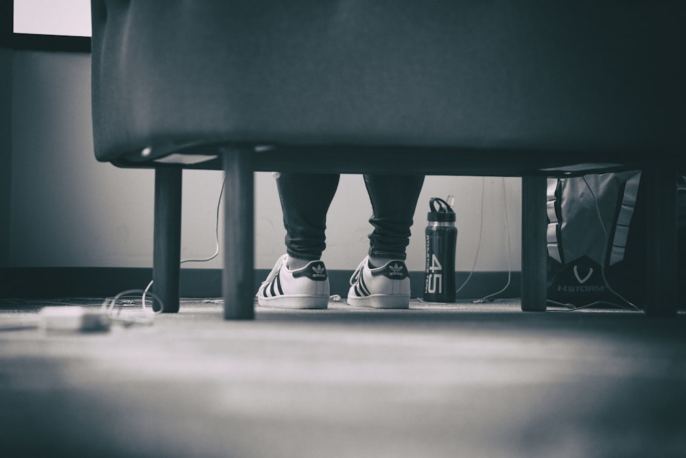 grayscale photo of person wearing adidas Superstar sitting down