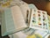 An open book with text in two columns lies on a cloth with a decorative leaf pattern. A notebook with colorful geometric letters spelling 'YOU ARE ENOUGH' and '1 PETER 2:9' is placed on top of the book, and a pen rests between the pages.