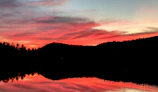 A breathtaking sunset over a calm lake with silhouetted trees.