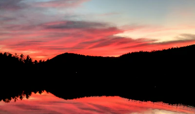 A breathtaking sunset over a calm lake with silhouetted trees.