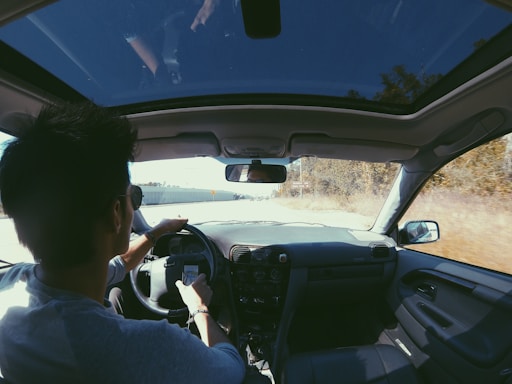 A friendly driving instructor helping a young learner behind the wheel on a sunny day.