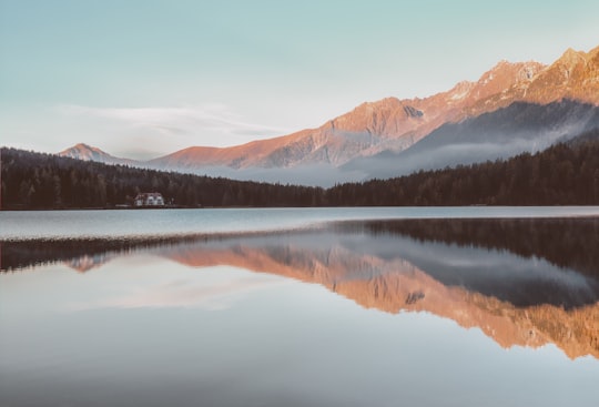 house near the forest and lake with mountains at the distance during day in Antholzer See Italy