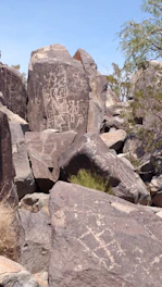 A panoramic view of ancient rock carvings in the Saudi desert under a clear blue sky.