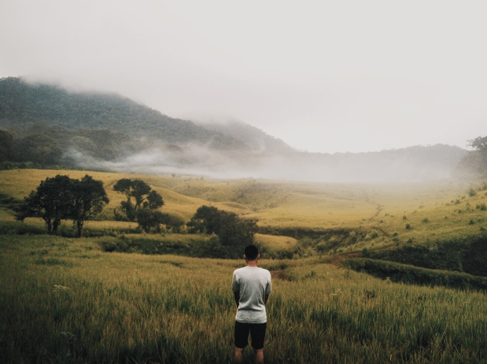 man facing grass field and trees near mountain