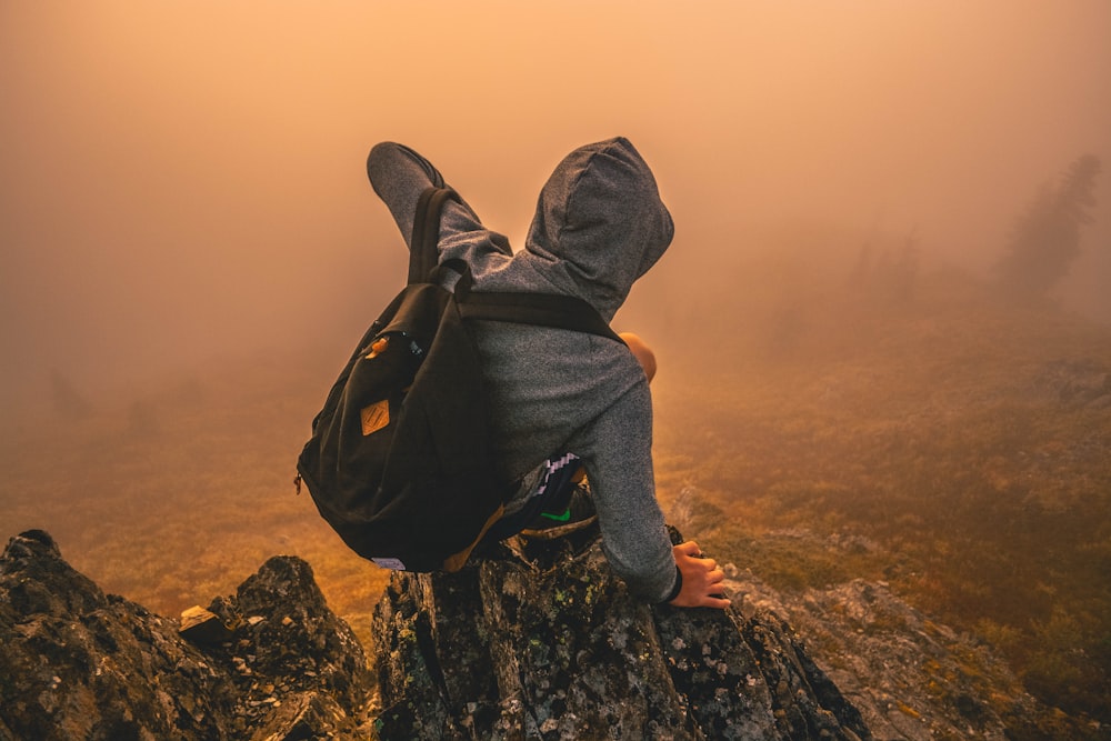 man in gray hoodie sitting on mountain during daytime