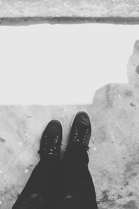 A pair of black sneakers on a rough, textured concrete surface. The image is in black and white, adding a minimalist and classic feel.