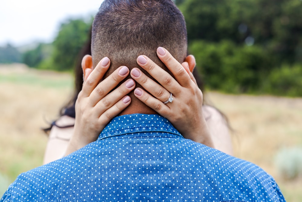 woman holding man's head near trees during daytime