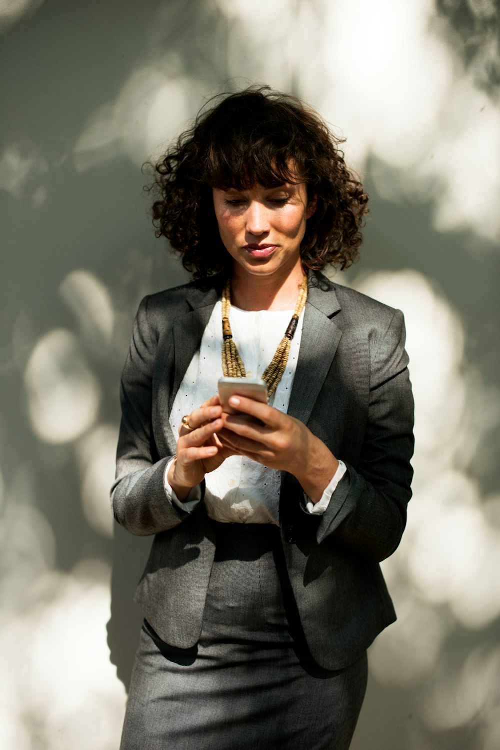 woman in black suit holding smartphone behind wall