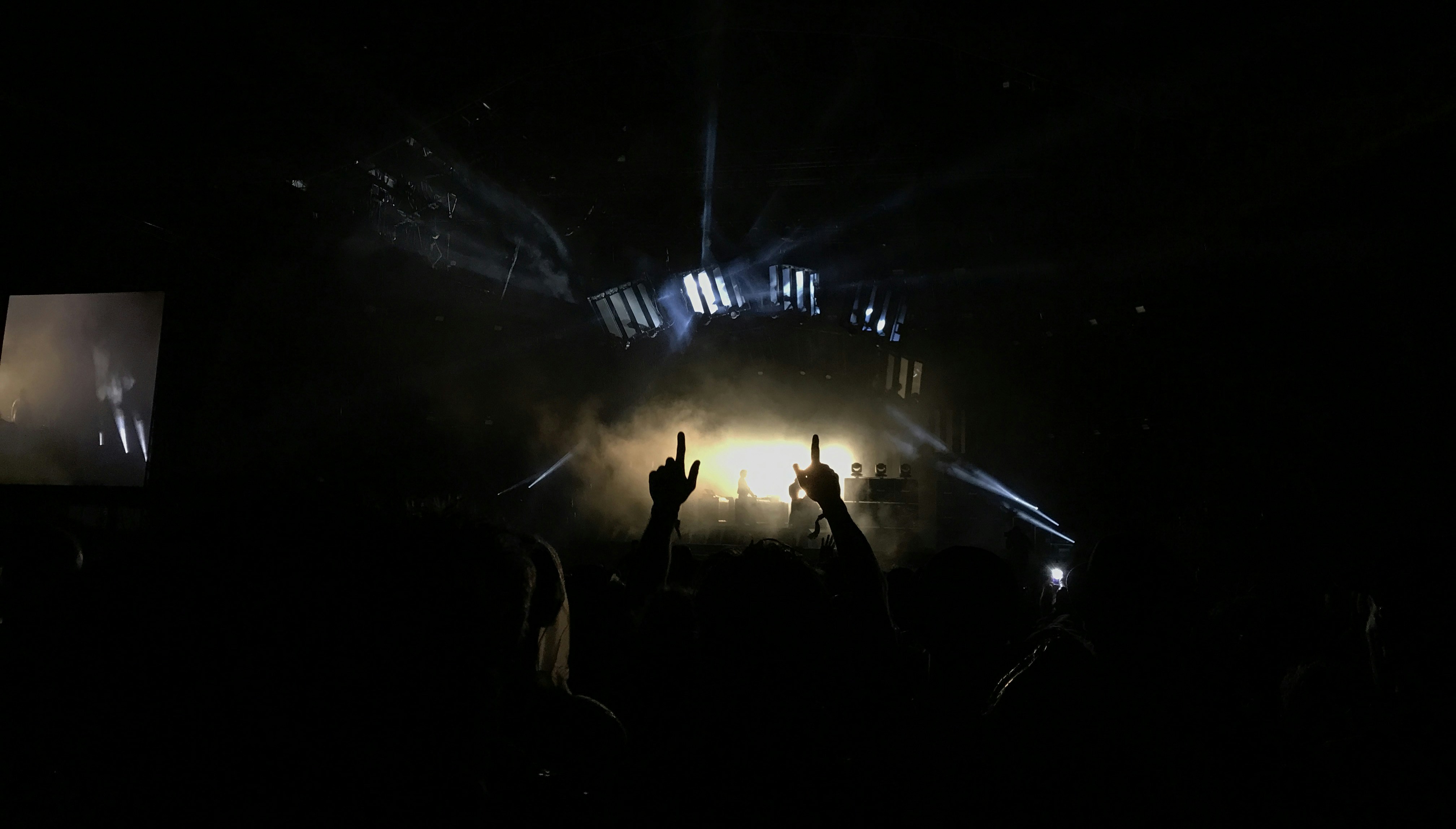 Concert crowd with hands raised and stage lights beaming in dark venue