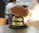 A hand is reaching towards a shiny, metallic desk bell set on a counter. The background is blurred, indicating a busy environment, likely in a reception or service area.