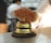 A hand is reaching towards a shiny, metallic desk bell set on a counter. The background is blurred, indicating a busy environment, likely in a reception or service area.