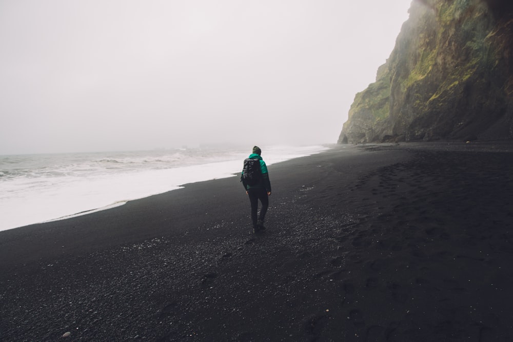 uomo che cammina sulla riva nera del mare