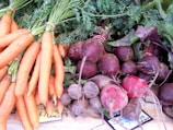 A collection of fresh vegetables displayed on a surface, including bunches of carrots with green tops and a variety of beets with stems and leaves attached.