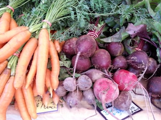 A collection of fresh vegetables displayed on a surface, including bunches of carrots with green tops and a variety of beets with stems and leaves attached.