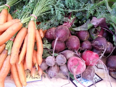 A collection of fresh vegetables displayed on a surface, including bunches of carrots with green tops and a variety of beets with stems and leaves attached.