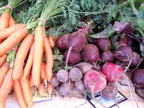 A collection of fresh vegetables displayed on a surface, including bunches of carrots with green tops and a variety of beets with stems and leaves attached.