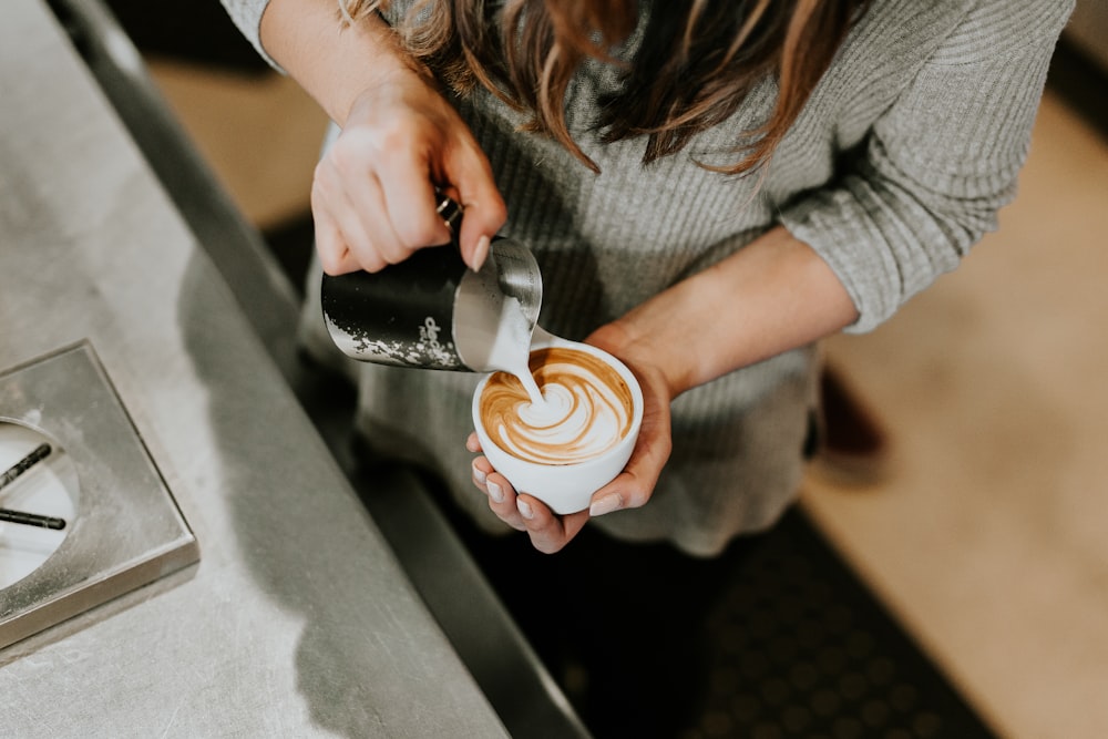 pessoa derramando xícara de café em xícara de cerâmica branca