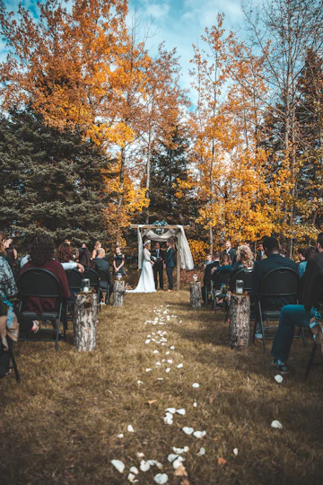 An outdoor wedding ceremony taking place beside trees turning to autumn colour