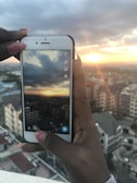 Person holding a smartphone taking a photo of a cityscape at golden hour