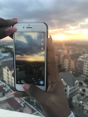 Person holding a smartphone taking a photo of a cityscape at golden hour