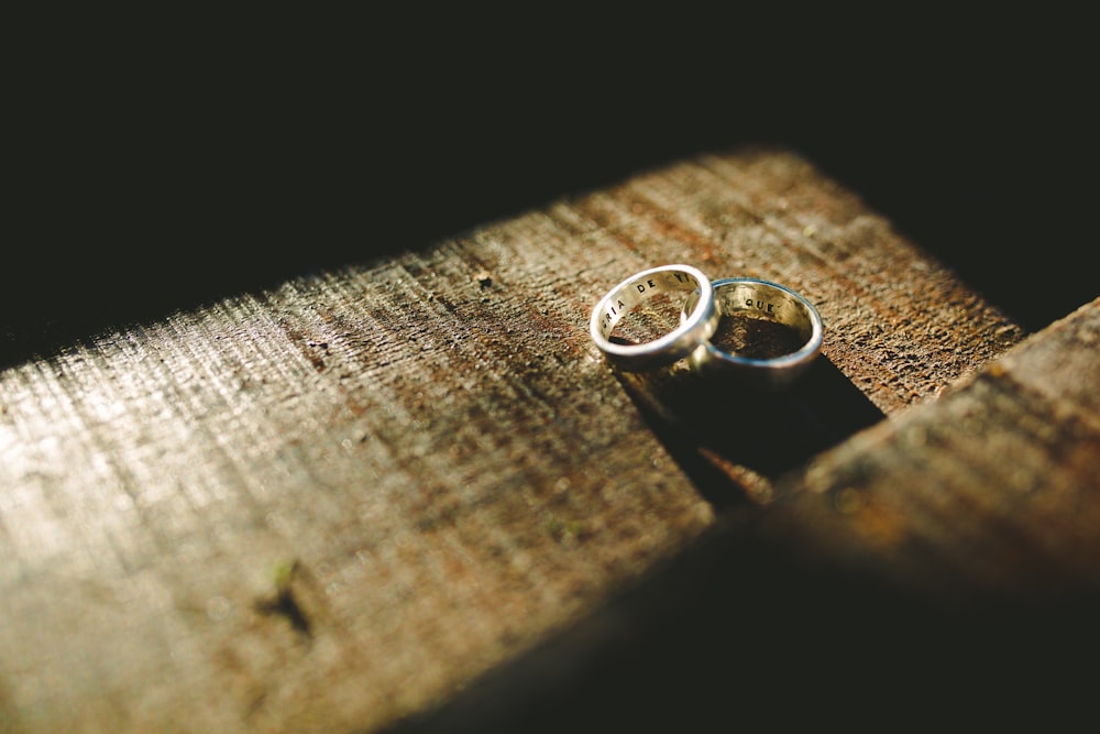 two silver-colored engagement rings on top brown surface