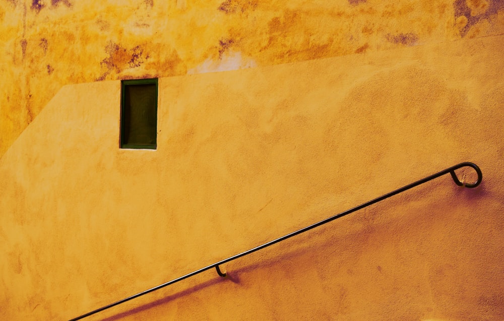 a yellow wall with a window and a metal handrail
