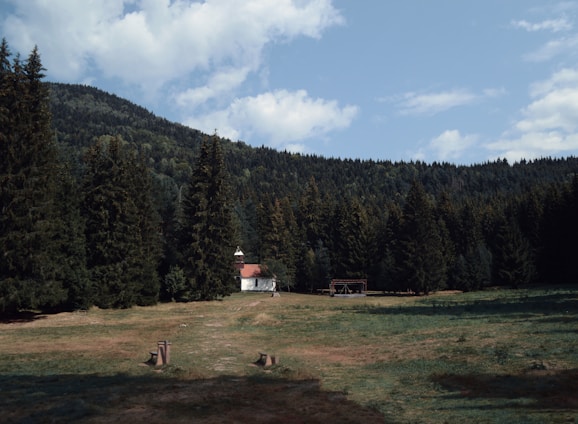 A serene chapel nestled in a lush green landscape under a clear blue sky.