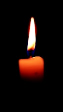 Elegant close-up of a softly glowing candle flame against a dark blue background.