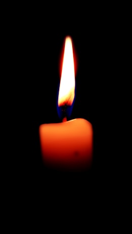 Elegant close-up of a softly glowing candle flame against a dark blue background.