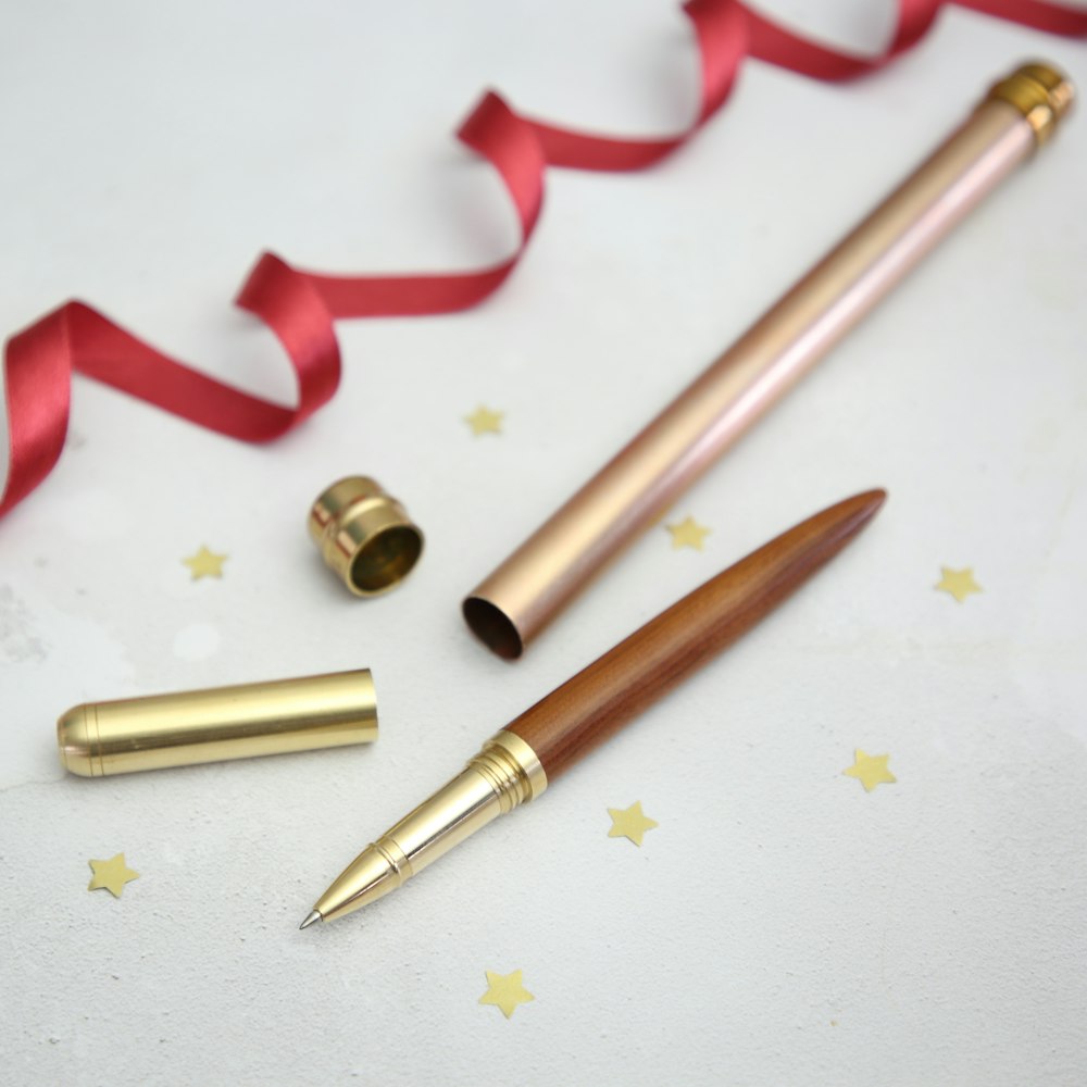brass-colored pen with case beside red ribbon on white surface