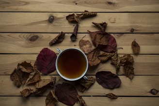 A warm cup of herbal tea surrounded by fresh leaves and spices on a rustic wooden table.