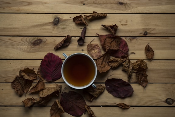 A cozy autumn scene with falling leaves and a warm cup of tea on a wooden table.