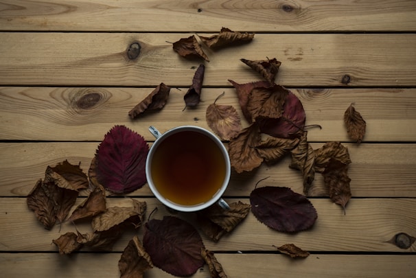 A warm cup of herbal tea surrounded by fresh leaves and spices on a rustic wooden table.