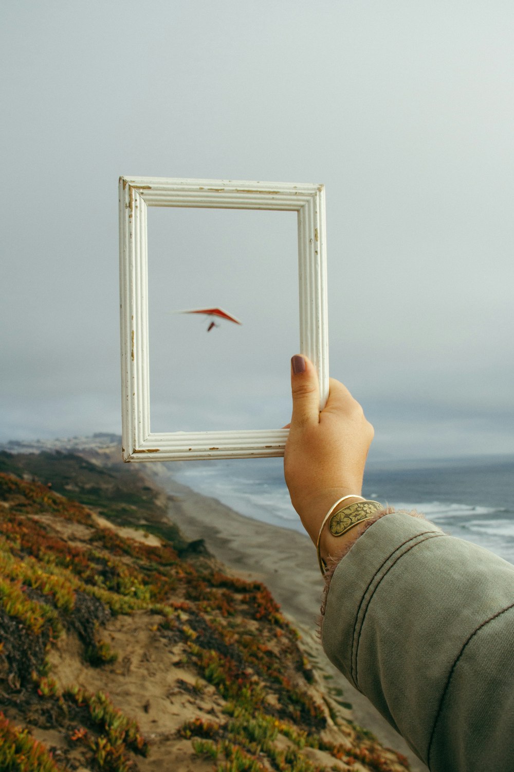 person holding rectangular white photo frame standing on rock formation near body of water