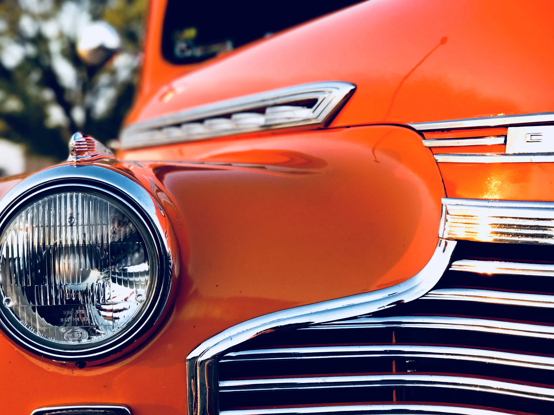 Close-up shot of a classic car's polished chrome details reflecting the vibrant event atmosphere.