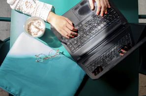 Close-up of Cory's hands typing on a laptop with coffee and notes nearby.
