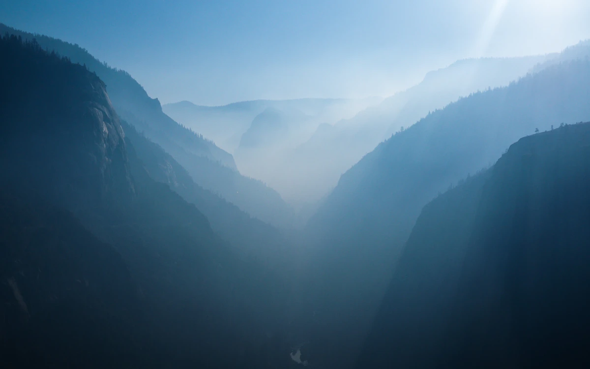 Aerial view of a misty mountain valley between tall granite cliffs with rays of light filtering through — the dramatic landscape found in major U.S. national parks