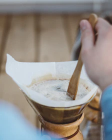 Barista gently stirring freshly brewed coffee in a clear glass cup.