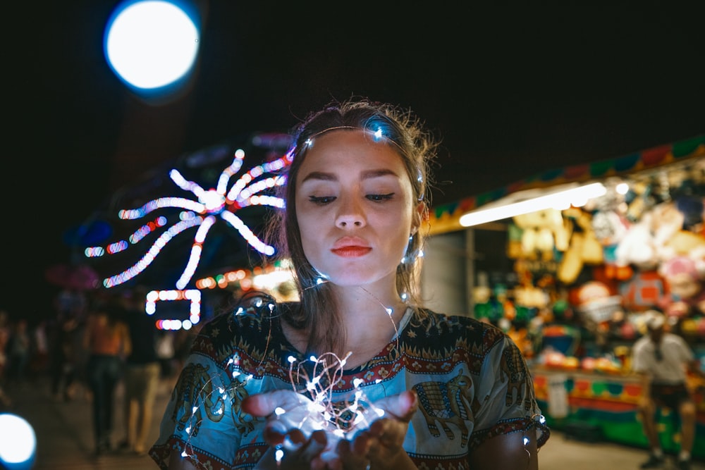 mujer con camisa multicolor sosteniendo luces de cadena encendidas