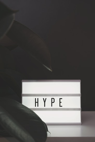 A lightbox with the word 'HYPE' illuminated in bold letters, set against a dark background with large green leaves partially in view.