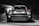 A sleek, modern vehicle parked in a dimly lit, industrial-looking garage. The car has a distinctive design with large, round headlights and a bold front grille. The lighting creates dramatic shadows and highlights on the car's surface, emphasizing its contours.