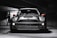 A sleek, modern vehicle parked in a dimly lit, industrial-looking garage. The car has a distinctive design with large, round headlights and a bold front grille. The lighting creates dramatic shadows and highlights on the car's surface, emphasizing its contours.